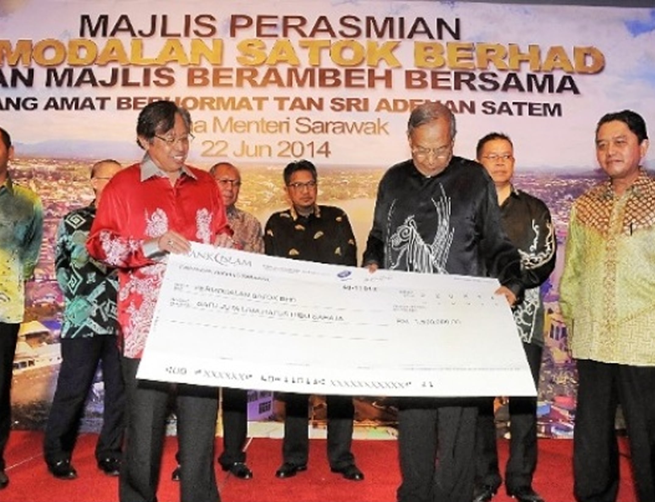 Group of men on stage holding ceremonial check under event banner, dressed formally in a celebratory setting.