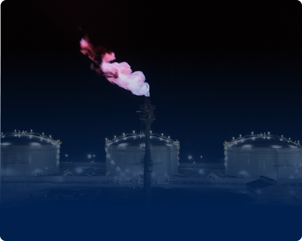 Night industrial scene with three lit storage tanks and a flare stack emitting pink-white flame.