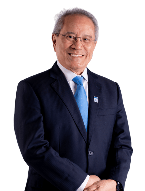 An older individual in a navy suit and blue tie, smiling confidently with glasses, set against a black background, exuding warmth and assurance.