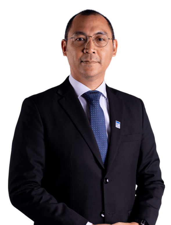 Man wearing dark suit, glasses, and blue tie with name badge against black background; confident and poised.